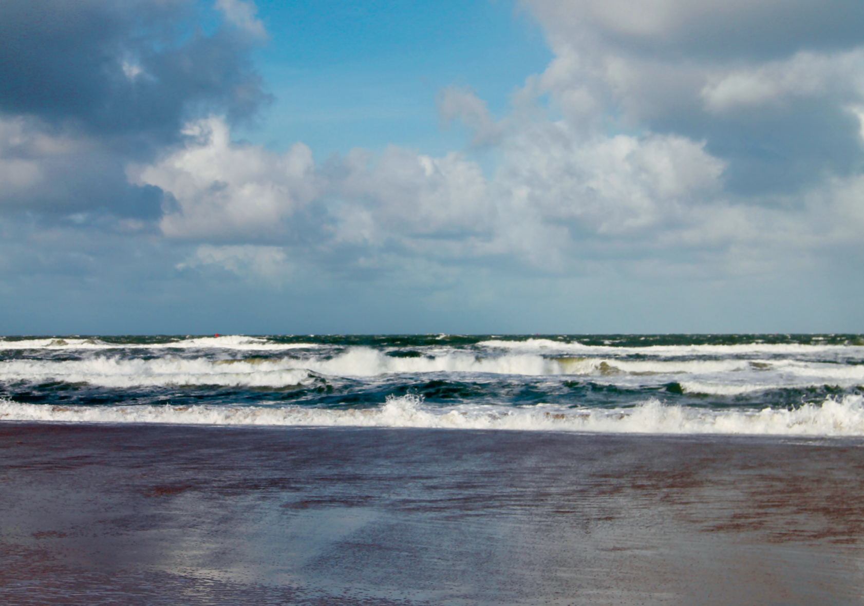Golven aan het strand van Vlieland onder een bewolkte blauwe lucht.